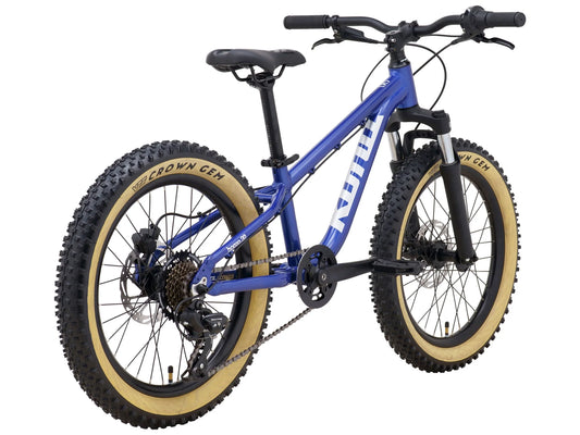 Kona Honzo 20 youth mountain bike in blue with tan sidewall Vee Crown Gem tires and black components, three-quarter rear view with drivetrain